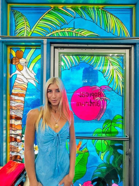 Woman in blue dress against colorful tropical stained glass